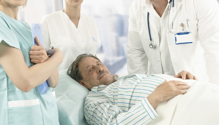 Elderly male patient lying in hospital bed wearing pyjama, medical team around.