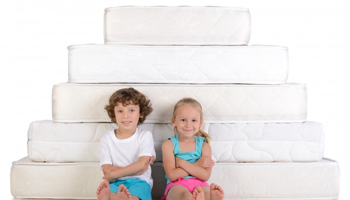 Young children sitting on lots of mattresses isolated on white background