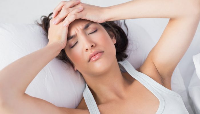 High angle view of a sleepy young woman suffering from headache with eyes closed in bed at home