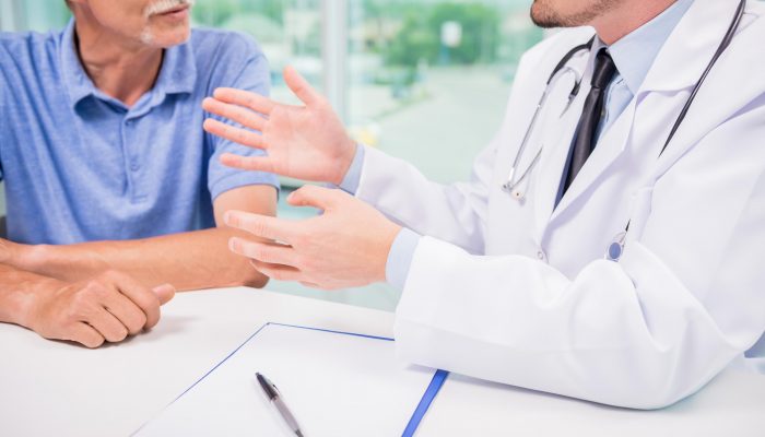 Male doctor talking with patient seriously at clinic. Close-up.