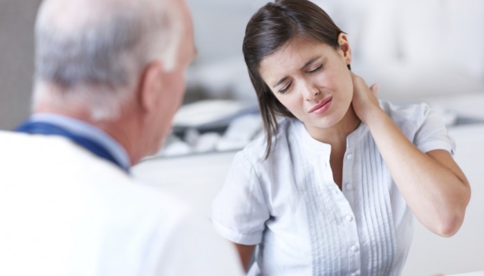 Young woman wincing with pain in a consultation with her doctor - copyspace