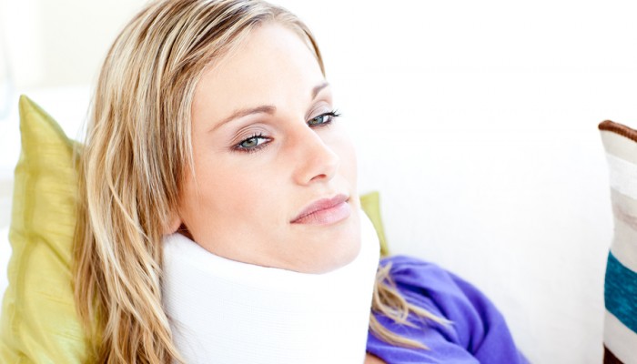 Beautiful woman wearing neckbrace lying on a sofa against a white background