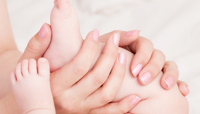 hands of amother massaging her baby's feet, in bed at home