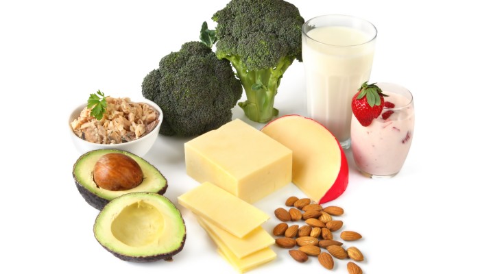 Calcium-rich foods on white background. Includes avocado salmon broccoli milk yogurt cheeses and almonds.