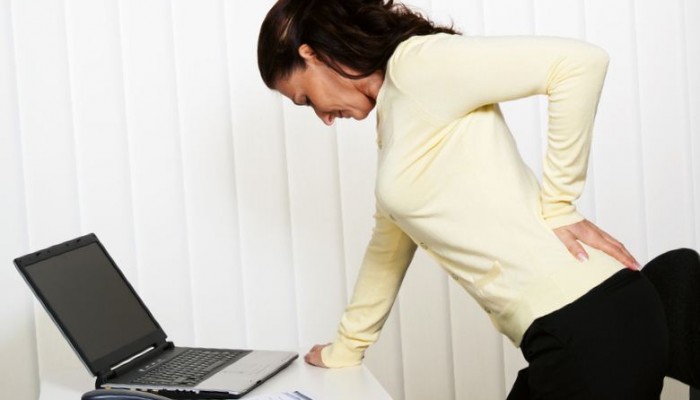 Woman with back pain of the intervertebral disc with office work at the desk.