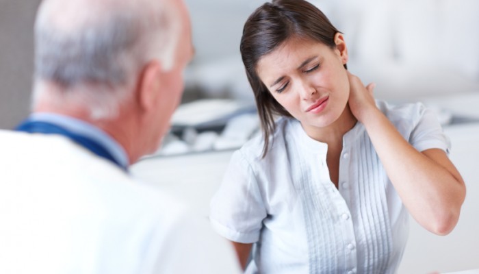 Young woman wincing with pain in a consultation with her doctor - copyspace