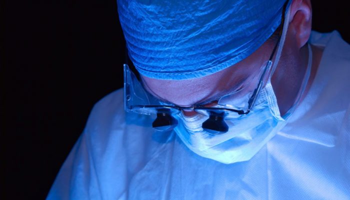 Surgeon or doctor wearing magnifying glasses to work. Lit from beneath with a black background.