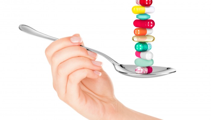 Hand holding a spoon with pills isolated on white background